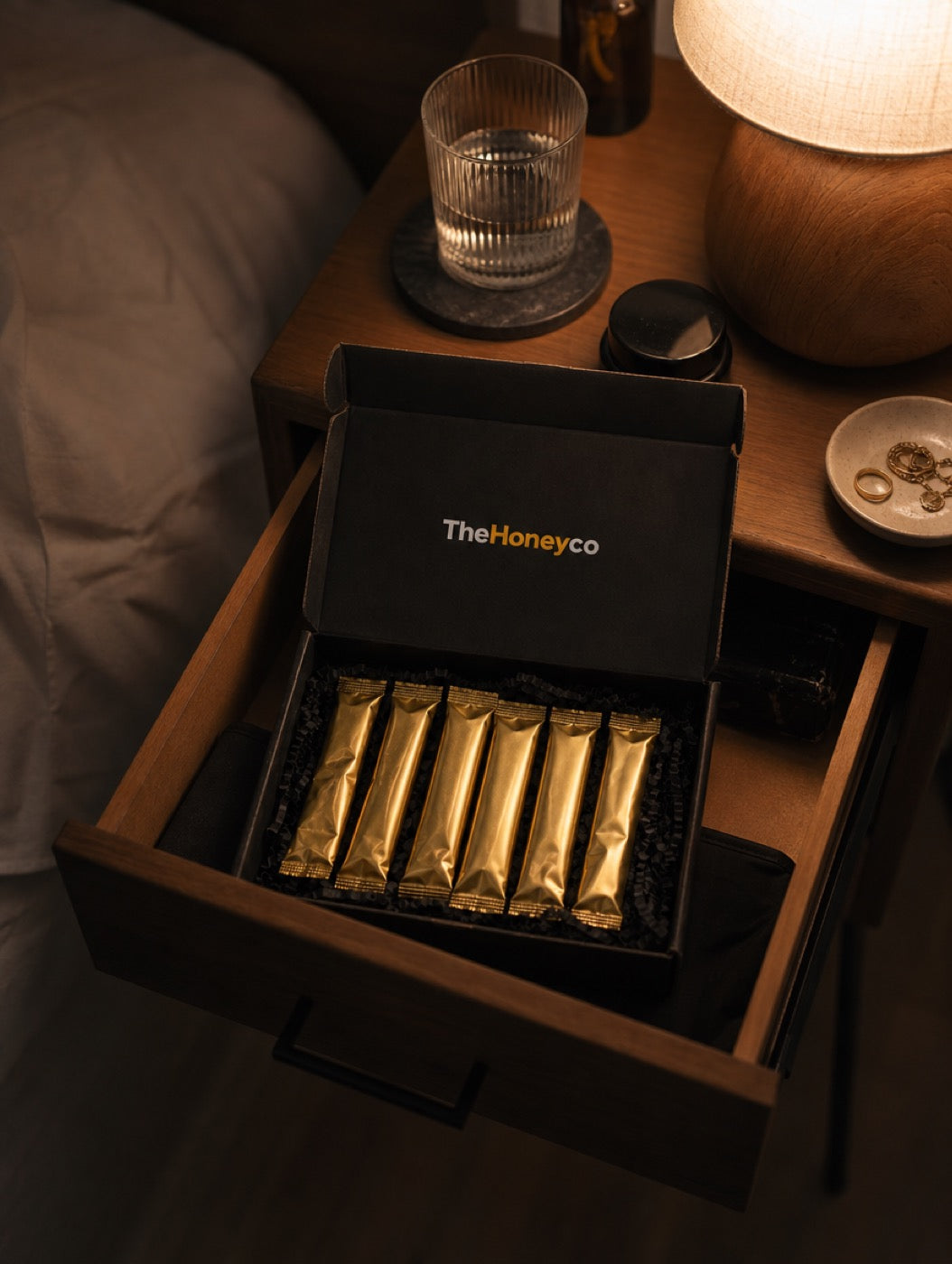 A TheHoneyCo box, open, on a bedside table at night