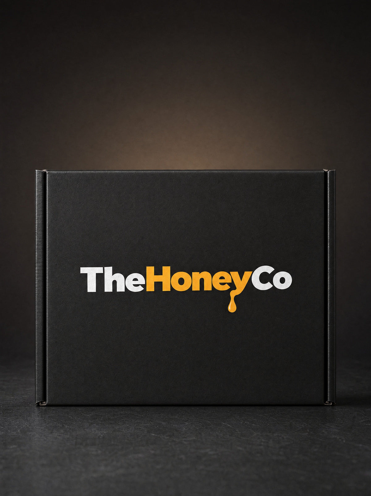 The front of a closed black TheHoneyCo box with the gold honey-drip wordmark